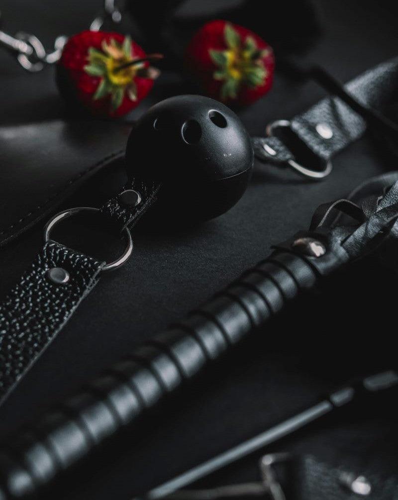 Accessori BDSM eleganti disposti su un tavolo in velluto scuro, con dettagli in metallo e pelle pregiata, atmosfera raffinata.