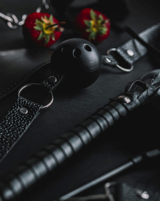Accessori BDSM eleganti disposti su un tavolo in velluto scuro, con dettagli in metallo e pelle pregiata, atmosfera raffinata.